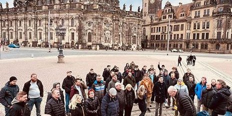 Eine große Gruppe von Menschen versammelt sich auf einem Platz vor einer beeindruckenden historischen Architektur.