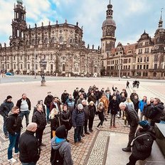 Eine große Gruppe von Menschen versammelt sich auf einem Platz vor einer beeindruckenden historischen Architektur.