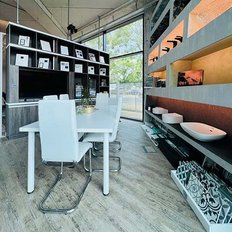 Ein moderner Essbereich mit einem weißen Tisch und Stühlen, umgeben von eleganten Regalen und großen Fenstern.