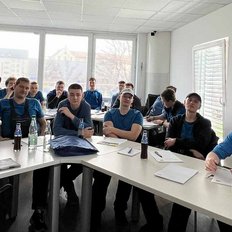 Eine Gruppe junger Männer sitzt in einem modernen Klassenraum und hört aufmerksam zu, während sie Notizen machen.