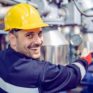 Ein Anlagenmechaniker mit einem Bauhelm, vor einer Heizungsanlage