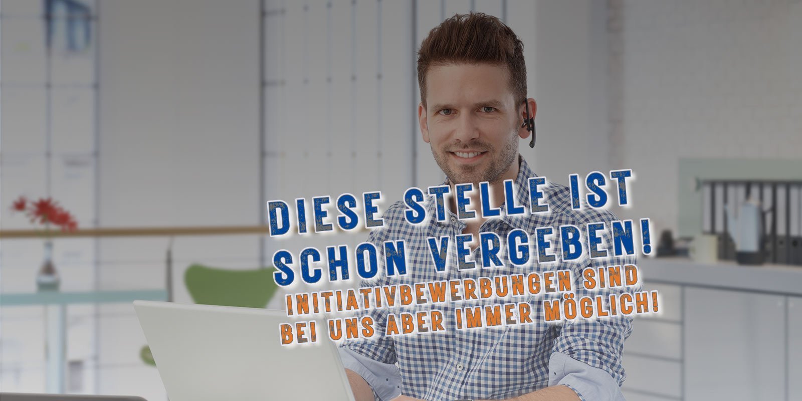Ein lächelnder Mann mit Headset sitzt an einem Schreibtisch, während er an einem Laptop arbeitet, umgeben von modernen Büromöbeln.